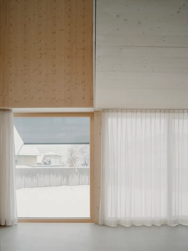 Window opening framing snowy landscape beyond a sheer curtain and plywood paneled walls