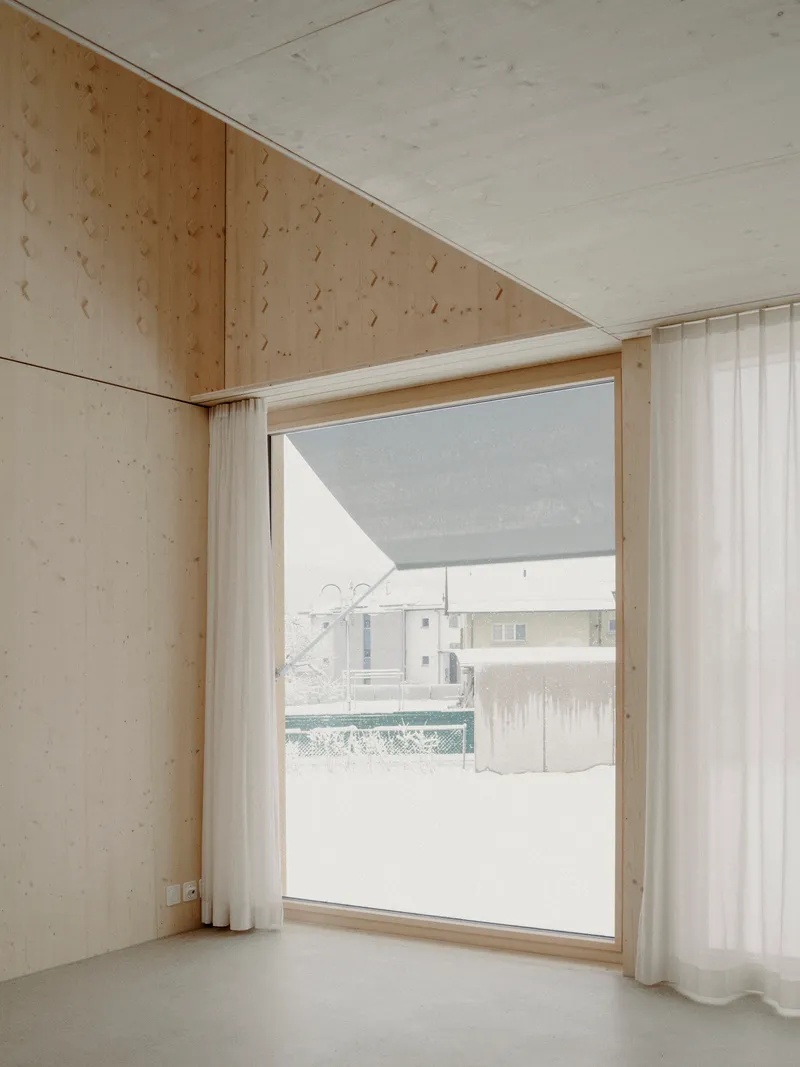 Light plywood interior corner with floor-to-ceiling window framing a snowy courtyard view
