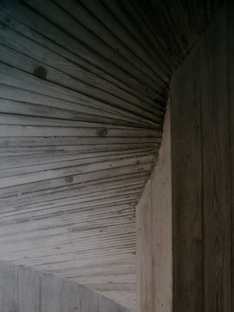 Close-up of ribbed timber ceiling meeting a board-formed concrete wall at the corner