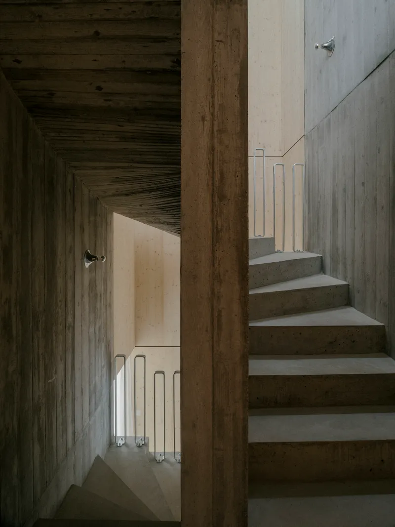 View through timber doorway showing concrete stairs ascending alongside a corridor with tube lighting below