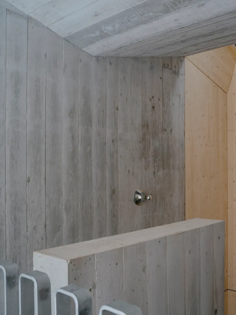Board-formed concrete wall with a single sconce above a low concrete bench