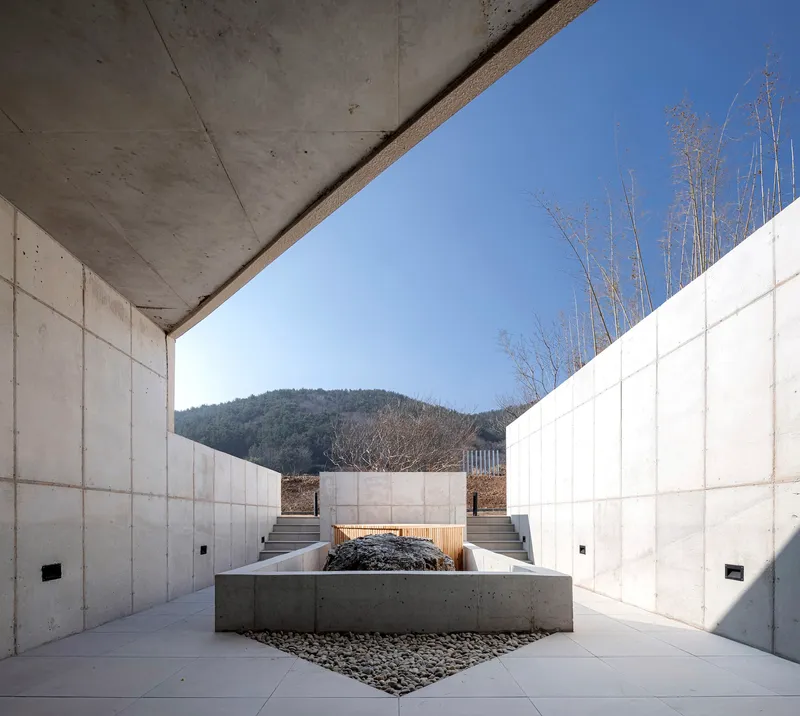 Concrete courtyard with central planting bed framed by tall walls and a mountain view