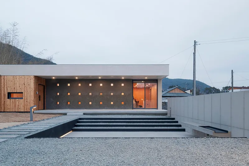 Entry facade with perforated concrete wall and wide stairs at dusk under overcast sky
