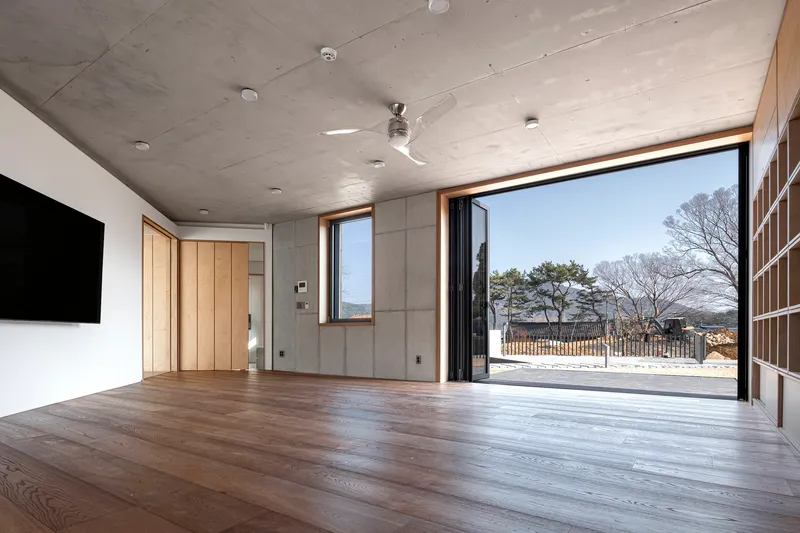 Living room with wide timber flooring and concrete ceiling opening to a courtyard through full-height glazed doors