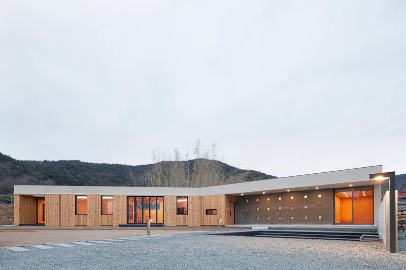 Horizontal timber-clad facade with scattered punched windows and illuminated concrete porch at dusk