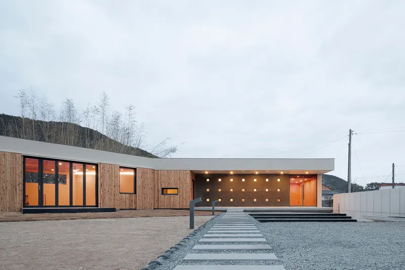 Horizontal facade combining timber cladding and white concrete with recessed square openings at dusk