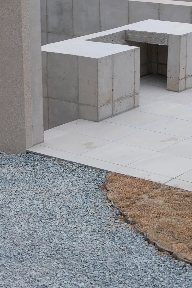 Board-formed concrete seating elements flanking gravel and paved stone ground plane