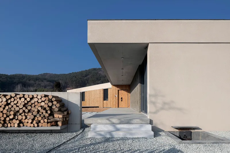 Entry steps leading to recessed entrance with stacked firewood wall and distant timber building