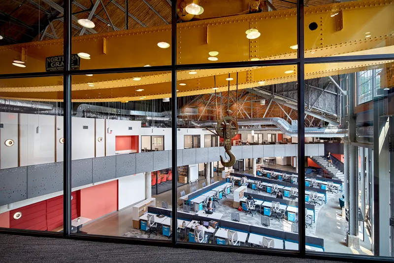 View through glazed partition wall overlooking the open workspace and yellow-painted crane beam at upper level
