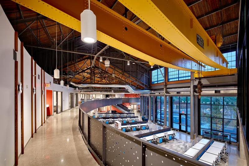 Corridor with perforated metal balustrade running along the upper level under yellow-painted structural beams at dusk