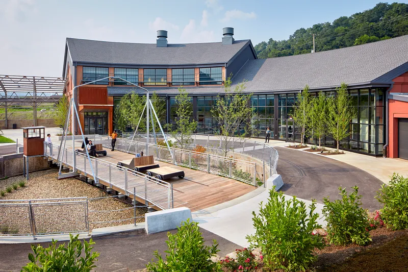 Elevated terrace with timber decking and cable railings, planted beds with young trees and swings between metal frames