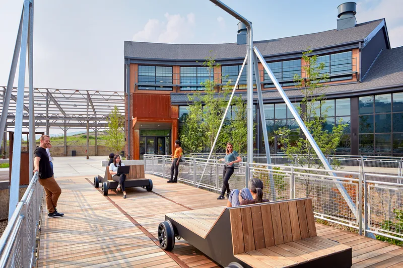 Timber deck terrace with cable mesh railings, metal swing sets and visitors seated on benches under a blue sky