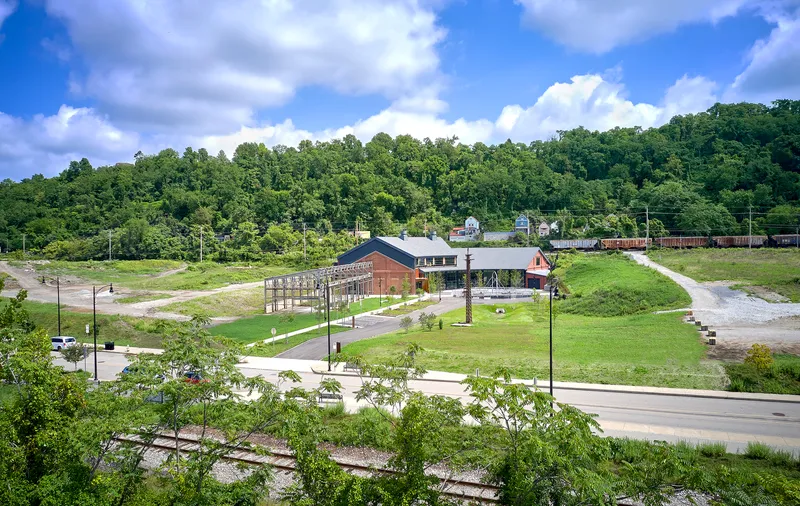 Wide view of the campus set in a green valley with young trees lining the access road and wooded hillside beyond