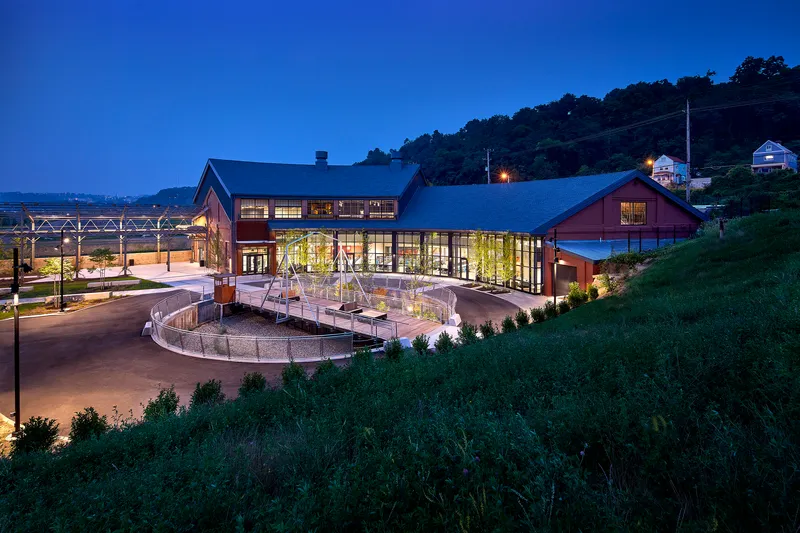 Glass-walled entrance with timber-framed gabled roofs and circular drive at dusk with hillside beyond
