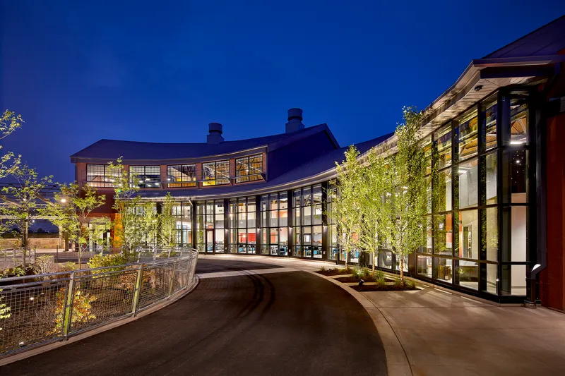 Curving entry drive with illuminated glass facades and planted courtyard under evening sky