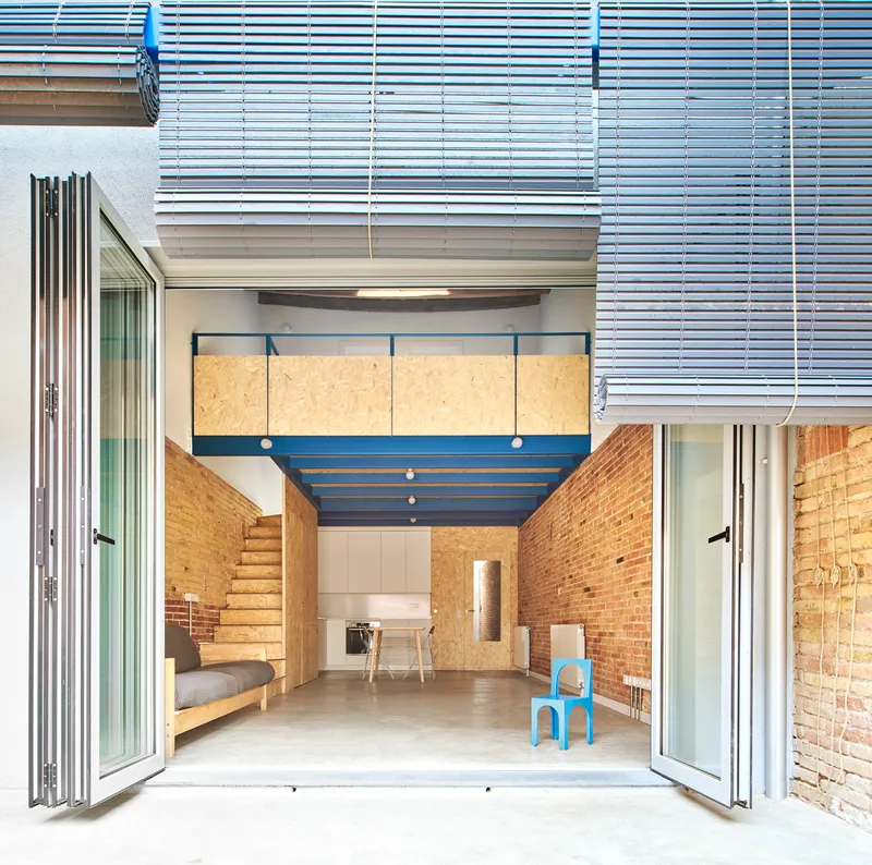 View from courtyard through open folding doors to blue steel mezzanine beneath metal louvered canopy