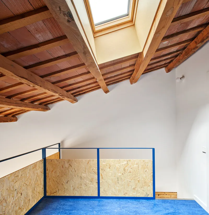 Upper level room with exposed timber ceiling beams, blue metal railing and oriented strand board panels below a skylight