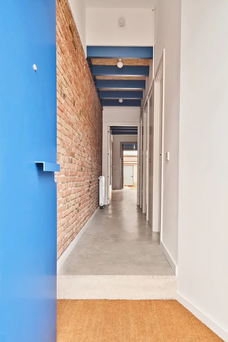 Narrow corridor with exposed brick wall painted blue on one side and polished concrete floor