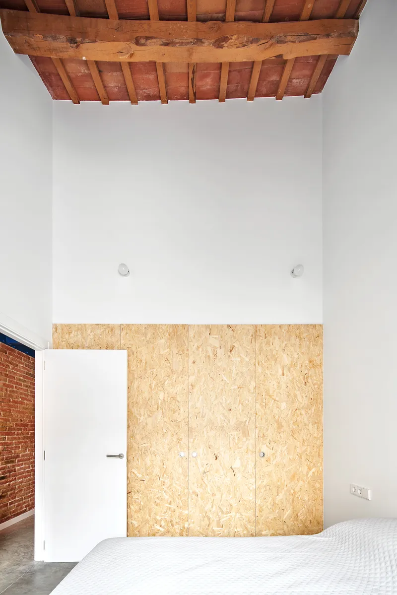 Bedroom with oriented strand board storage wall insert beneath exposed timber ceiling beams