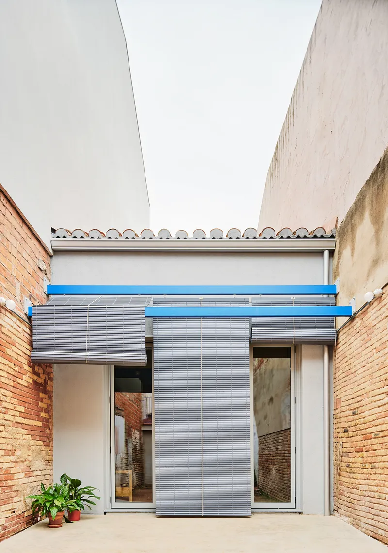 Courtyard framed by brick walls with corrugated metal shutters and blue painted steel lintel under overcast sky