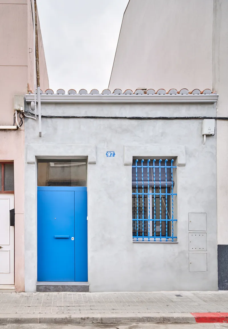 Street facade with bright blue door and barred window on a white stucco wall