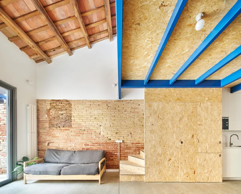 Interior living space with exposed brick wall and oriented strand board ceiling panels on blue joists