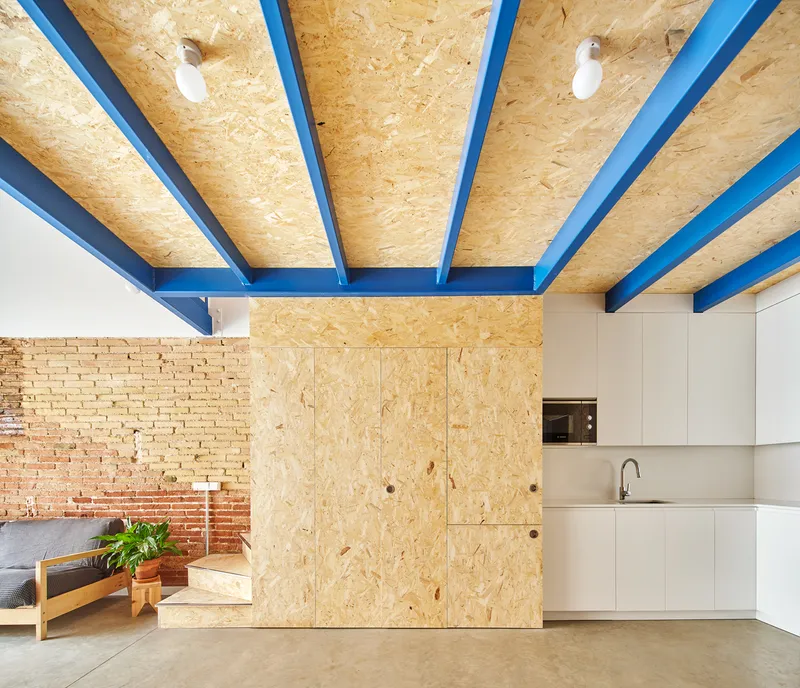 View of kitchen with oriented strand board ceiling and exposed brick wall under blue structural beams