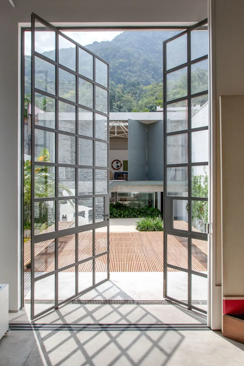Open steel-framed glass doors leading to a timber deck courtyard with mountains visible beyond