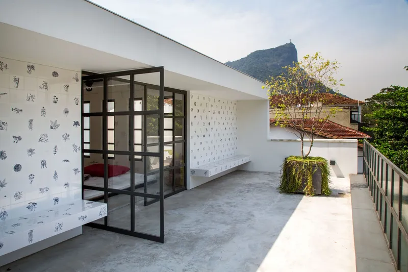 Concrete terrace with black steel framed glass doors opening to a bedroom beneath a distant mountain peak