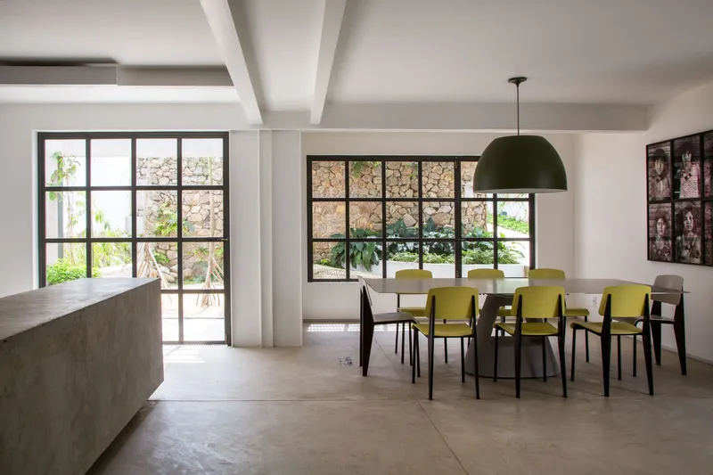 Dining area with concrete kitchen island and steel-framed windows overlooking a stone wall garden