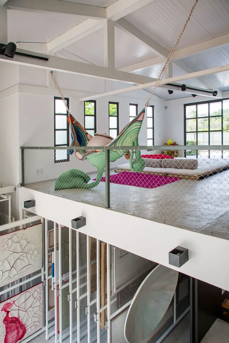 Upper-level lounge with exposed timber ceiling beams, wire mesh balustrade and suspended hammock