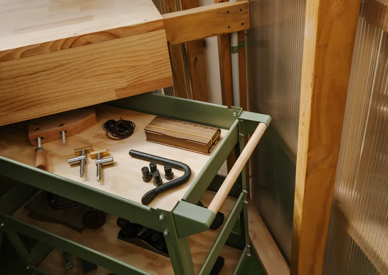 Open drawer of green metal tool cart displaying hardware and hand tools on plywood base