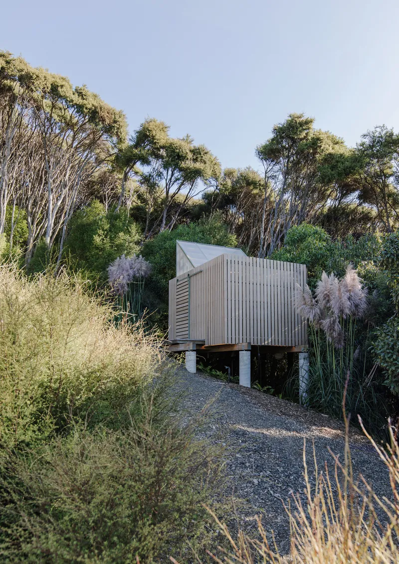 Elevated timber pavilion on concrete piers accessed by a gravel path through native grasses
