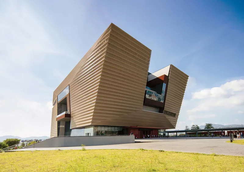 Horizontal banded facade with cantilevered volumes rising above a grass lawn under clear skies