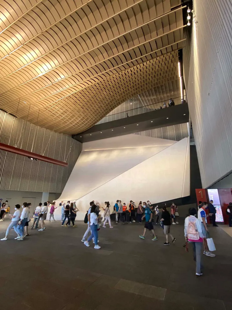 Interior lobby with vaulted timber ceiling and white sculptural wall with visitors gathered below