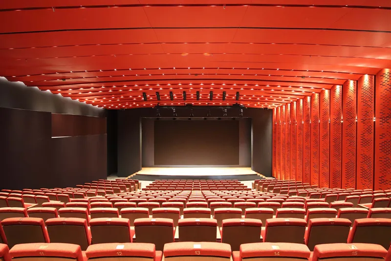 Auditorium interior with textured red acoustic ceiling panels and matching upholstered seating facing the stage