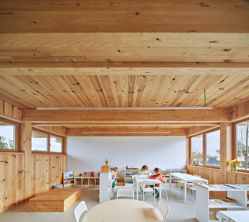 Interior classroom with exposed timber ceiling beams and children seated at tables