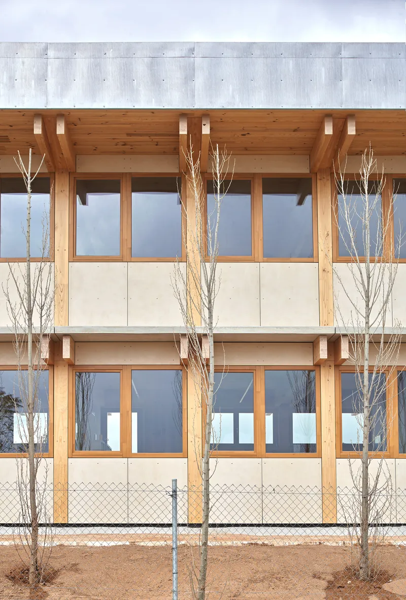 Two-story timber facade with horizontal banding and bare winter trees behind chain-link fence