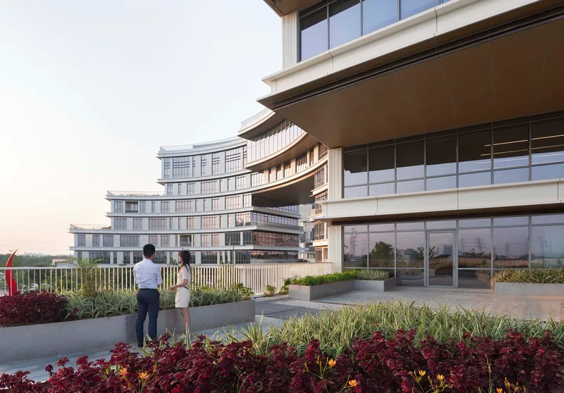 Rooftop terrace with planted beds and two people looking toward horizontal facade bands at dusk