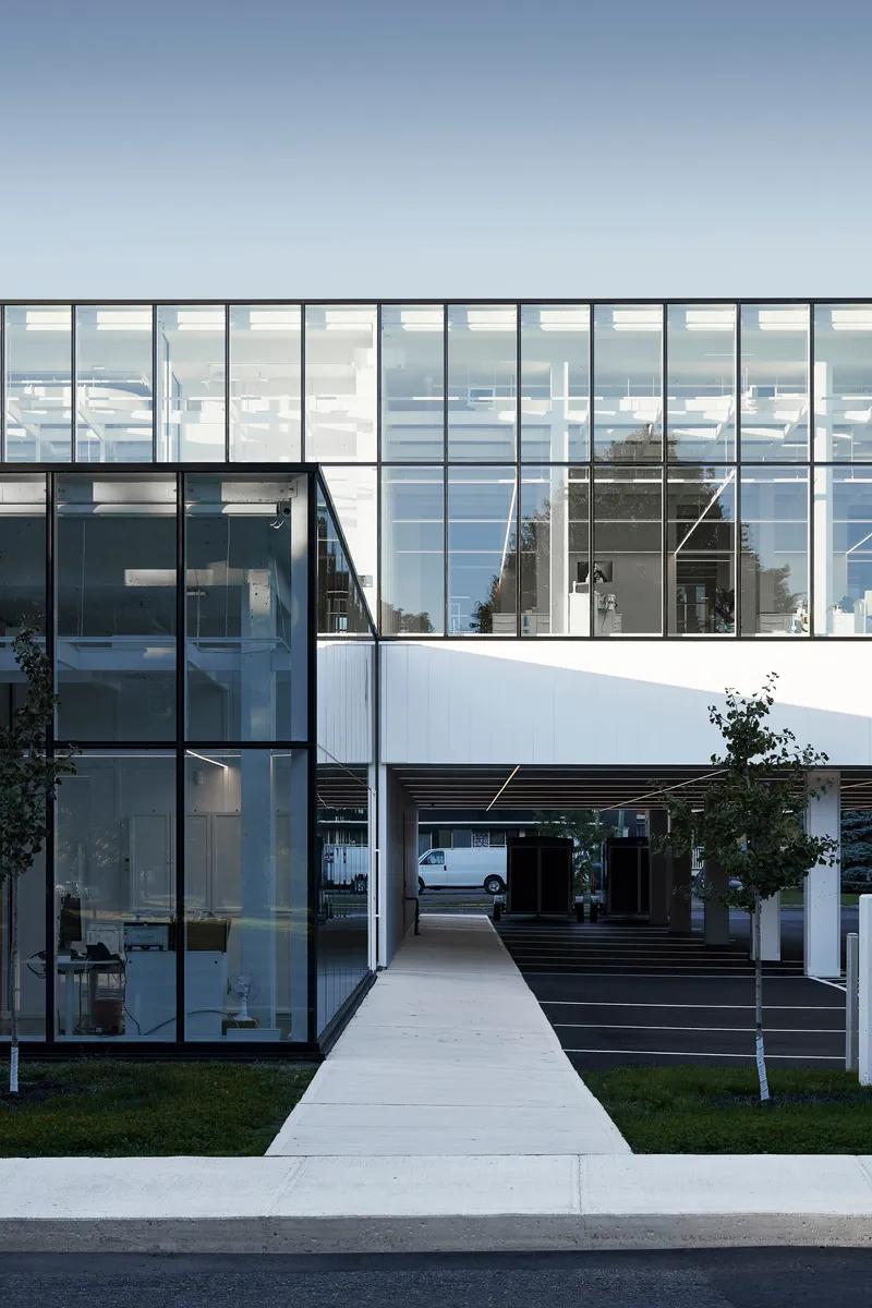 Concrete pathway leading between glass facades and a timber-clad volume at twilight
