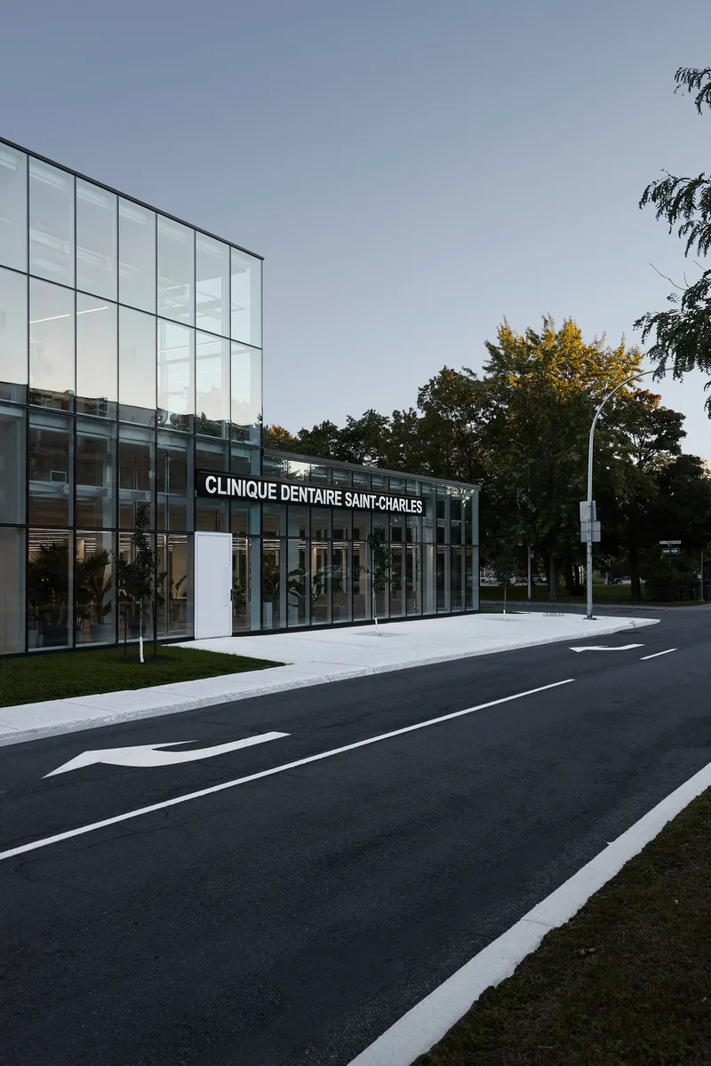 Street view of the glazed entrance facade flanked by young trees at dusk