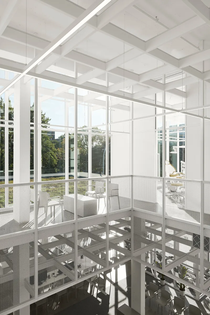 White steel framework and perforated metal mezzanine floor with double-height glazed walls overlooking garden