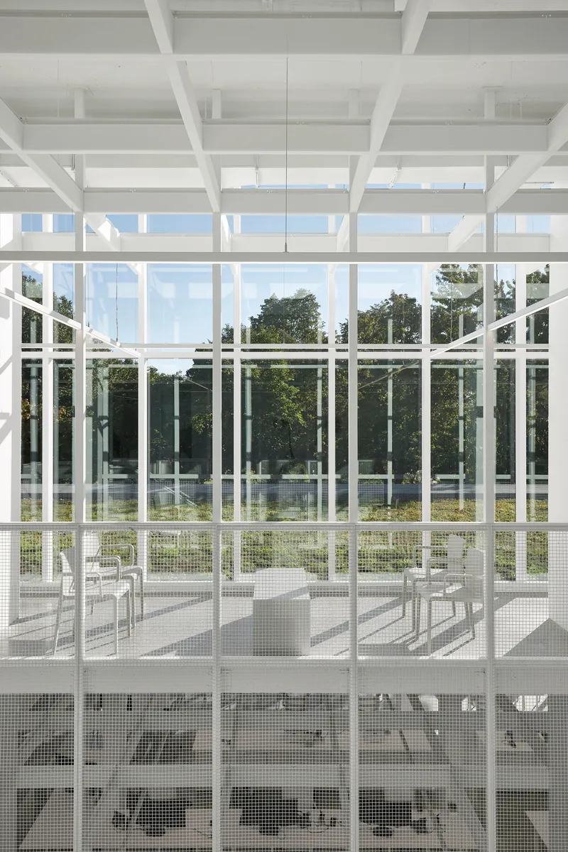 Layered white steel frames with perforated metal guardrails beneath coffered ceiling and clerestory glazing