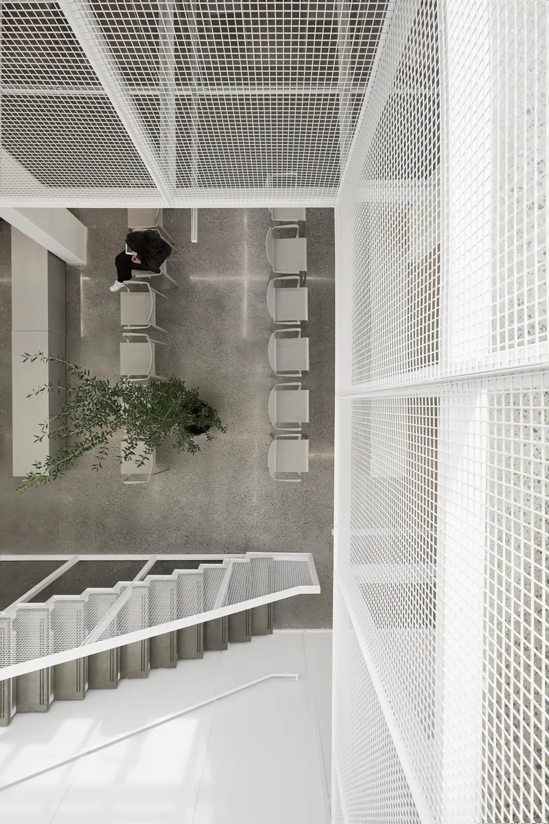 Top-down view of a multi-story atrium with white perforated metal balustrades and a person seated at grey tables