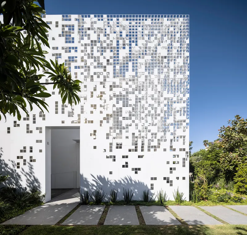 White facade with gradient pixelated tile pattern framed by garden plants and concrete pavers