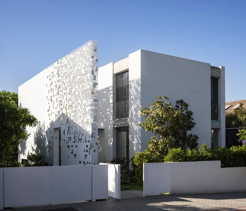 Street view of white volumes with pixelated tile screen and planted trees along pavement