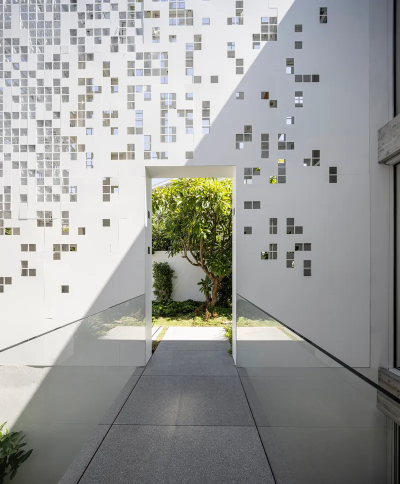Interior corridor with pixelated tile walls opening to courtyard tree through narrow passage