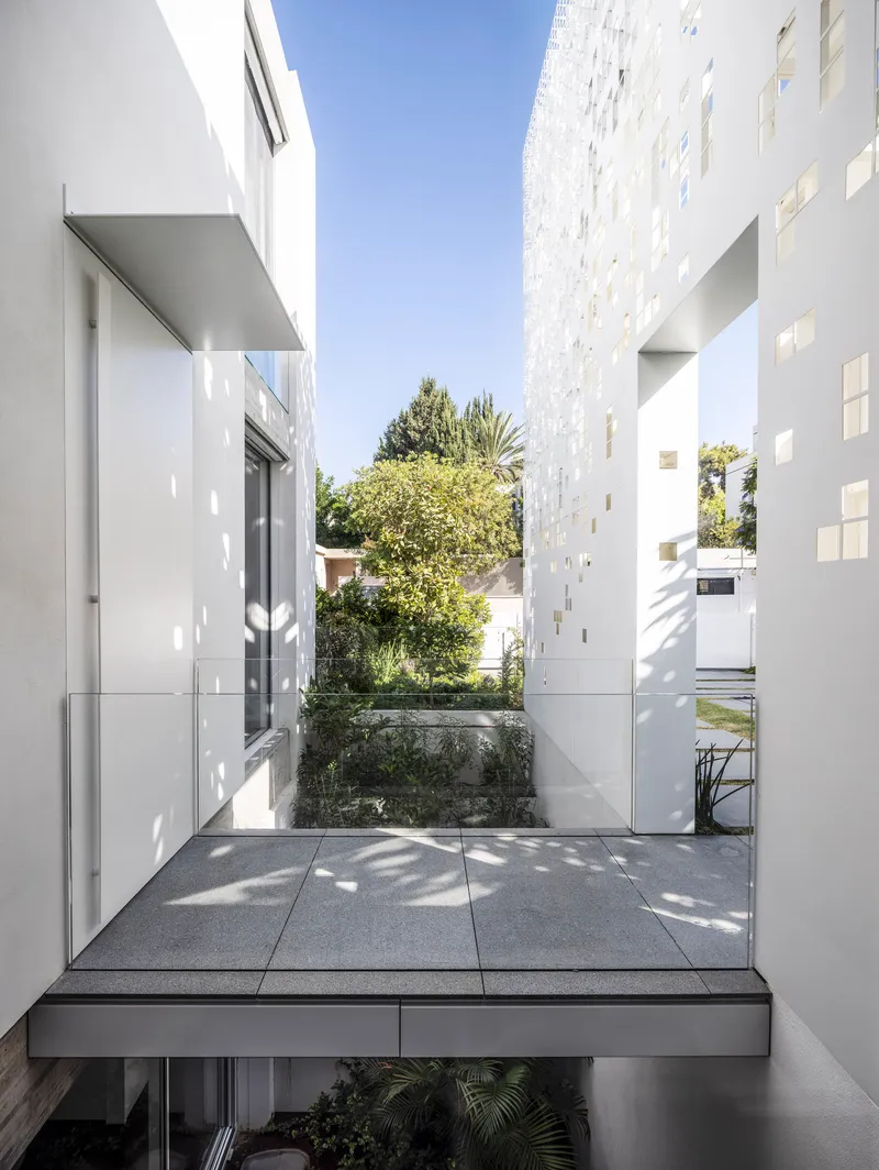 Terrazzo-paved terrace framed by white perforated screen walls with planted courtyard and dappled sunlight