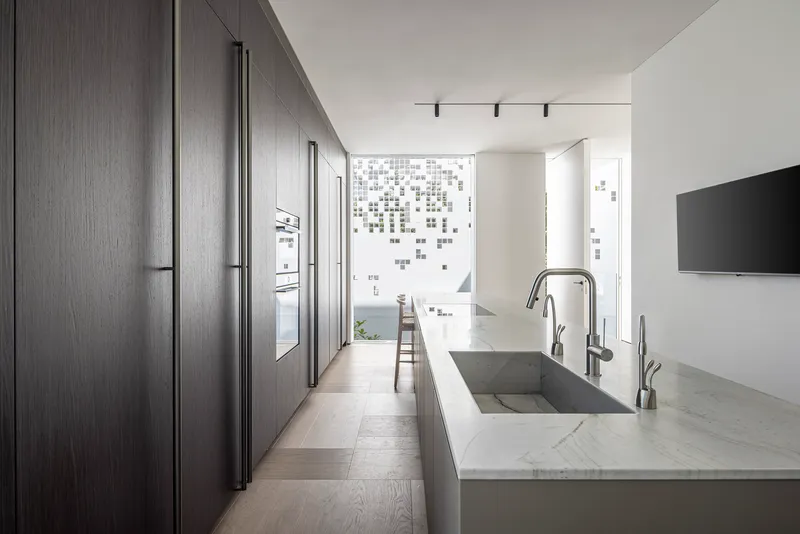 Galley kitchen with dark wood cabinetry and marble waterfall island facing perforated facade screen