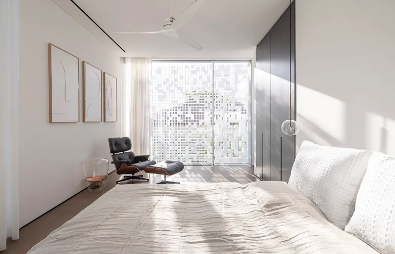 Bedroom with glazed wall behind dark timber wardrobe panels and afternoon light striping the floor